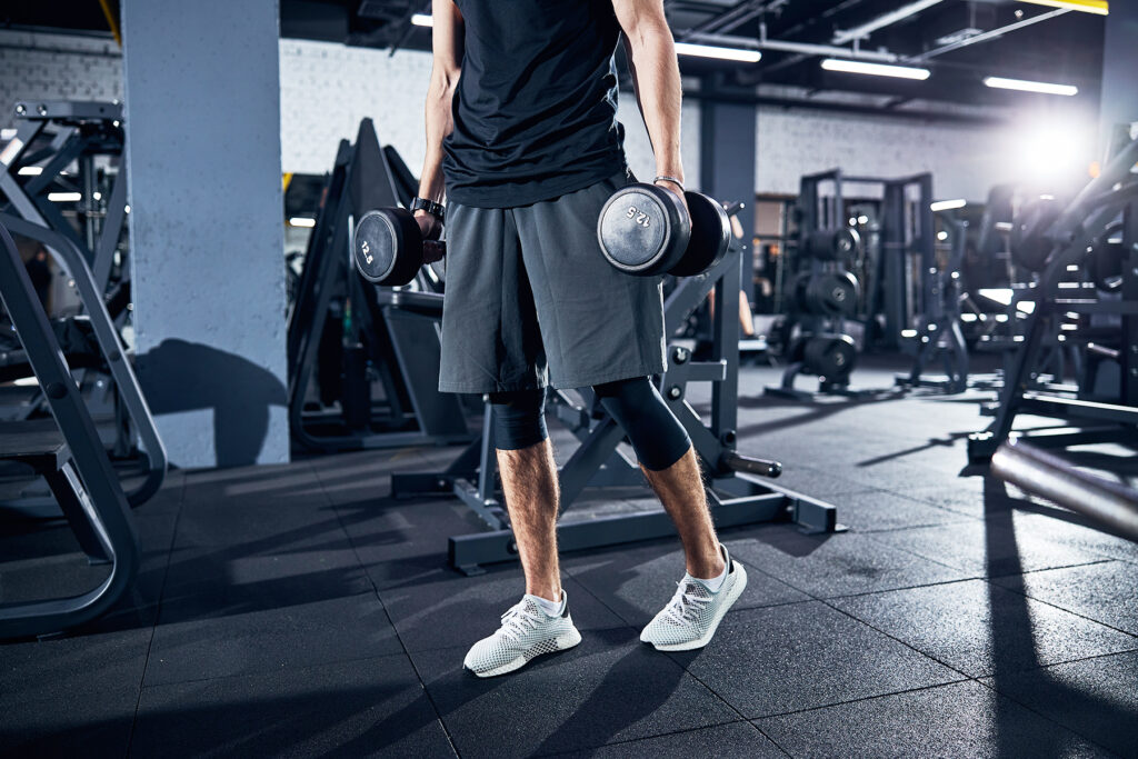 Cropped photo of a sportsman in shorts and white boots walking away with hand weights