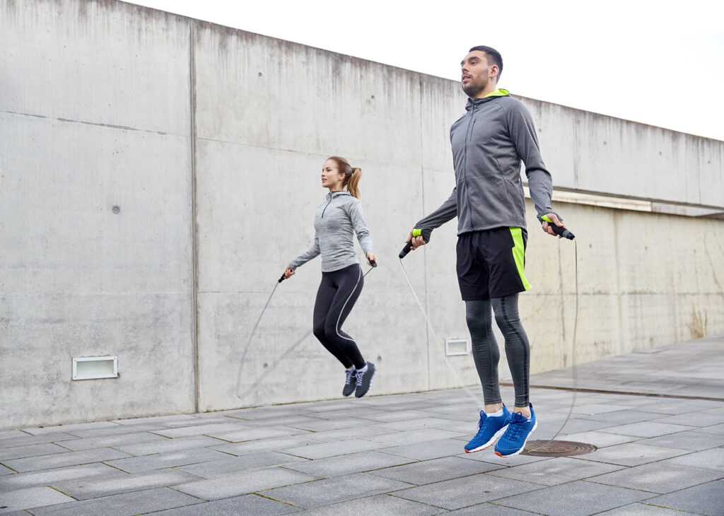 fitness, sport, people, exercising and lifestyle concept - man and woman skipping with jump rope outdoors